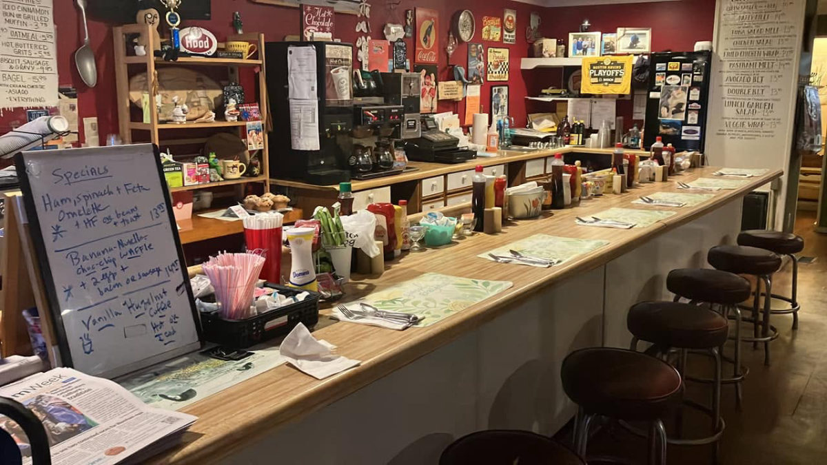 The counter at Riverside Cafe with stools, coffee, condiments, and a handwritten specials board